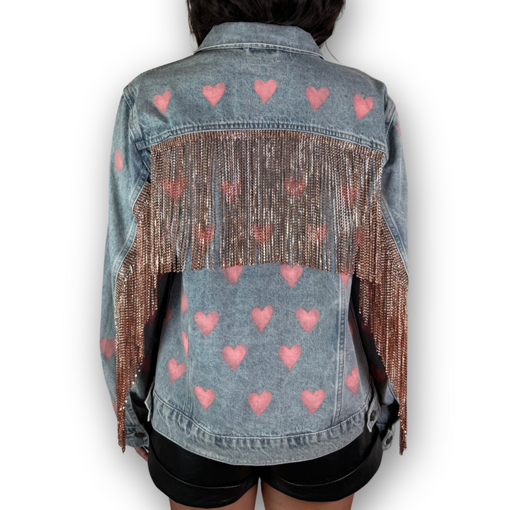 Denim jacket with pink heart patterns and fringe details on a white background