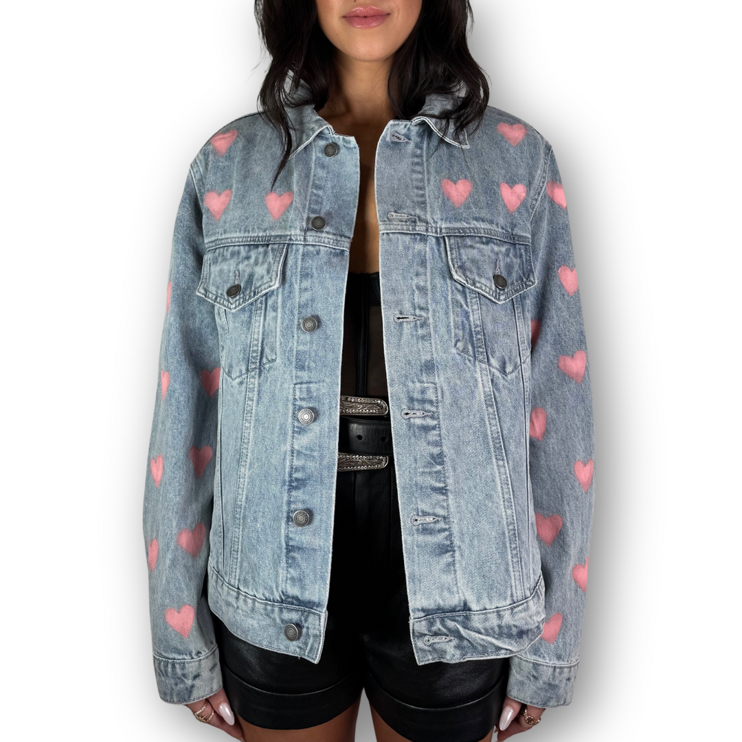 Denim jacket with pink heart patterns worn by a person on a white background